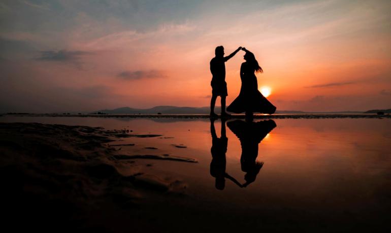 Coppia balla al tramonto sulla spiaggia, riflessa nell'acqua.