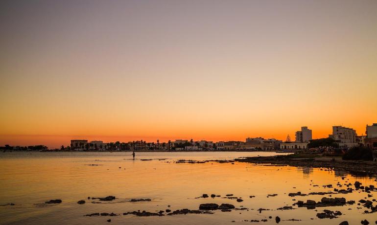Tramonto sereno su una costa tranquilla, cielo arancione e riflessi dorati sull'acqua.