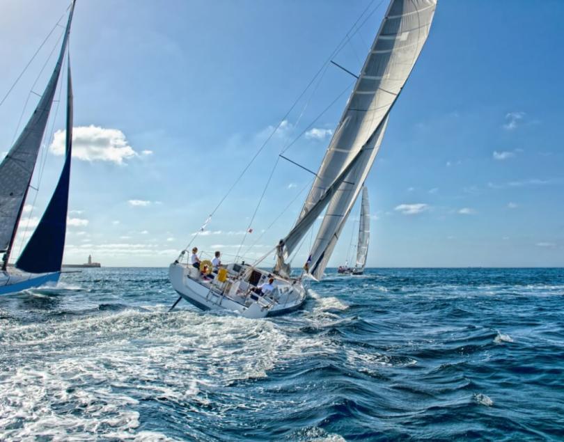 Regata di vela, barche inclinate, mare blu, cielo sereno, equipaggio in azione.